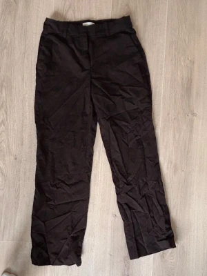 Svarta kostymbyxor från H&M - Säljer ett par svarta kostymbyxor från H&M med raka ben och klassisk passform. Byxorna har hyska och hake-stängning samt dragkedja. Materialet är en blandning av polyester, viskos och elastan vilket ger en skön stretch och snygg look.