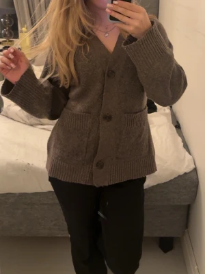 Brun kofta med stora knappar - Mysig brun kofta med v-ringning och stora knappar framtill. Koftan har två stora fickor och breda ribbade muddar vid ärmslut och nederkant. Perfekt för lager på lager och enkel att matcha med olika outfits.