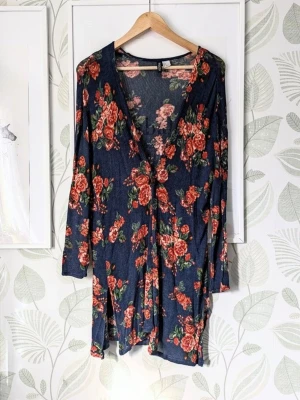 Längre Cardigan H&M Storlek S-M - Marinblå kofta med blommigt mönster i rött och grönt. Långärmad modell med djup v-ringning och avslappnad passform. Tillverkad i mjuk viskosblandning med lite stretch för extra komfort. Perfekt för dig som gillar en trendig och bekväm stil.
