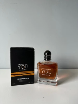Emporio Armani Stronger With You Intensely - Emporio Armani Stronger With You Intensely är en parfym med elegant, fyrkantig glasflaska och mörkbrun doftvätska. Flaskan har en rund, metallisk kork och stilren design. Förpackningen är svart med guldiga detaljer och tydlig logotyp. Volymen är 100 ml.