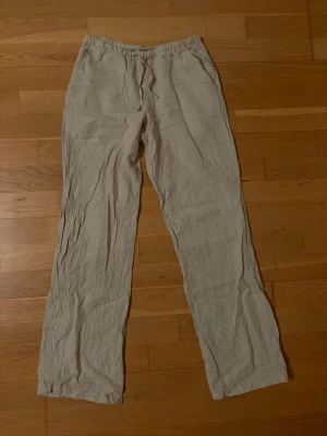 Beiga linnebyxor med resårmidja - Säljer ett par beiga linnebyxor med rak passform och resår i midjan. Byxorna är tunna och luftiga, perfekta för varma dagar. Materialet är klassiskt linne som ger en avslappnad vibe.