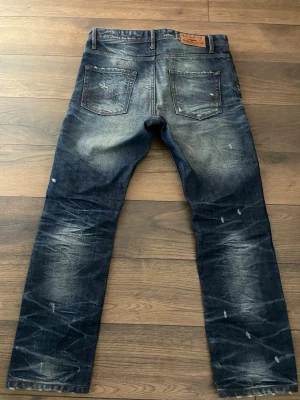 Mörkblå distressed jeans från Dsquared2 - Säljer ett par mörkblå jeans från Dsquared2 med slitningar och tvättade detaljer. Jeansen har raka ben, två bakfickor och en klassisk läderpatch i midjan. Materialet är denim i bomull och de har en trendig, sliten look.