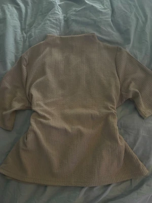 Beige ribbad topp från Pieces - Säljer en beige ribbad topp från Pieces med hög hals och trekvartsärm. Toppen har en mjuk struktur och är i ett stretchigt material som sitter snyggt på kroppen. Perfekt att styla med jeans eller kjol.