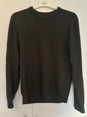 Mörkgrön stickad tröja - En enkel och stilren mörkgrå stickad tröja med rund halsringning och långa ärmar. Svårt att fånga färgen på bild men bild 1&5 ger rättvis färg.   100%  merinoull