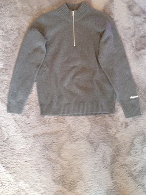 Half zip  - Mysig grå stickad tröja från Jack & Jones med hög krage och halv dragkedja framtill. Tröjan har ribbade muddar vid ärmslut och nederkant samt diskret logga broderad på ena ärmen. Perfekt för lager-på-lager och enkel att matcha.