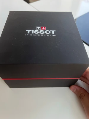 Tissot klocka Seastar 1000.  - Snygg Tissot-klocka med blå urtavla och matchande blå bezel. Armbandet är i blankt rostfritt stål och klockan har tydliga vita markeringar. Kommer i originalbox med Tissot-logga. Perfekt accessoar för dig som gillar stilrena detaljer.
