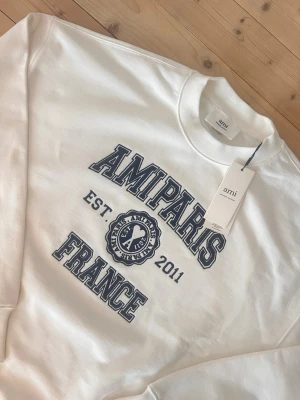 Ami Paris Tröja  - Snygg AMI Paris sweatshirt i krämvit färg med tydlig “AMI Paris France”-logga framtill. Helt ny med tags, aldrig använd. Mjuk och högkvalitativ med en avslappnad passform – perfekt för vardagsbruk.  Känn dig fri att skicka bud eller frågor 😊