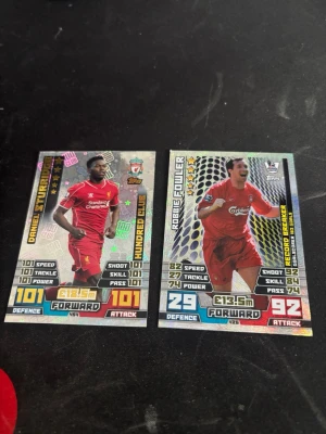 Match Attax Liverpool samlarkort - Två Match Attax samlarkort från Topps med Liverpoolspelare i röda matchställ. Kortens framsida har holografiska detaljer och visar statistik som speed, shoot och power. Baksidan har Match Attax-logga och Premier League-märke. Perfekt för samlare av fotbollskort.