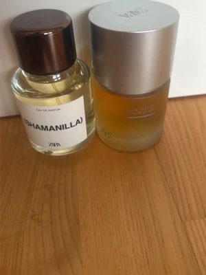 Zara Shamanilla & Ultra Glitch parfym - Två parfymer från Zara: Shamanilla i en rund glasflaska med mörkbrunt lock och tydlig vit etikett, samt Ultra Glitch Dystopia i en frostad glasflaska med silverfärgat lock. Båda har modern design och stilrena detaljer.