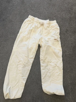 Vita mjukisbyxor från Puma - Säljer ett par vita mjukisbyxor från Puma med resår i midjan och dragsko för skön passform. Byxorna har avslappnad passform och resår vid bensluten. Perfekta för chill dagar eller träning. Puma-logga på vänster ben.