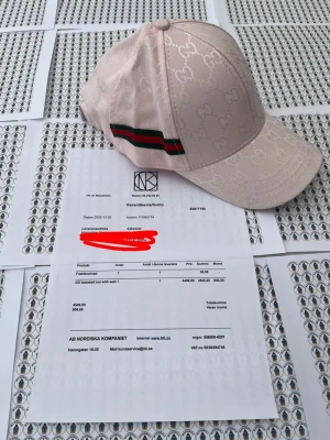 Ljusrosa keps från Gci med G-mönster - Säljer en ljusrosa keps från Gci med det klassiska G-monogrammet över hela kepsen. På sidan finns ett grönt och rött band som ger en ikonisk touch. Kepsen har böjd skärm och justerbar rem bak. Materialet är canvas med detaljer i bomull.