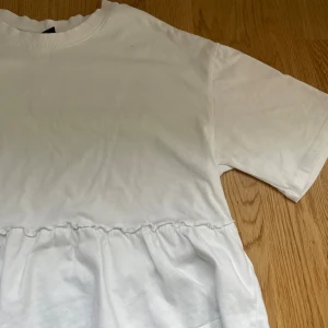 Vit volang topp med kort ärm - Supersnygg vit T-shirt med volang nedtill. Perfekt nu till våren och sommaren💕