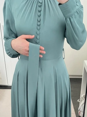 Ljusblå långklänning med knappar - Elegant ljusblå långklänning med långa ärmar, dekorativa klädda knappar framtill och ett matchande bälte i midjan. Klänningen har mjukt fallande tyg och fina veckdetaljer vid axlar och kjol. Perfekt för dig som gillar stilrena och klassiska plagg.Finns även i lila 💜 