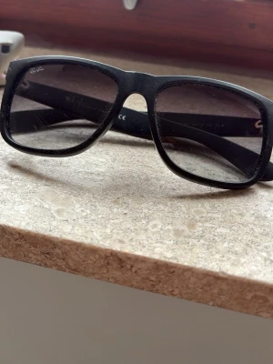 Rayban solglasögon  - Snygga svarta solglasögon med bred båge och klassisk form. Perfekta för att ge en cool touch till din outfit. Passar till alla tillfällen där du vill skydda ögonen mot solen.
