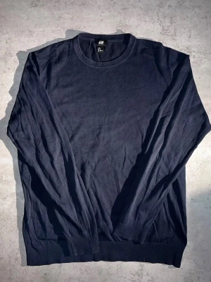 Mörkblå stickad tröja H&M - L - En stilren mörkblå stickad tröja från H&M med rund halsringning och långa ärmar. Tröjan har ribbade muddar vid ärmslut och nederkant. Perfekt för lager-på-lager och enkel att matcha med olika outfits.