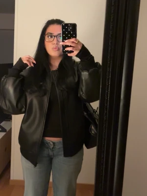 Svart oversized skinnjacka - Säljer en svart oversized skinnjacka med breda axlar och ribbade muddar vid ärmslut och midja. Jackan har dragkedja framtill och en cool, avslappnad passform som ger en trendig look. Perfekt för dig som gillar streetstyle och vill ha en statementjacka. Den är ifrån bikbok.