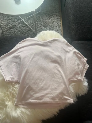 Ljusrosa t-shirt från Nelly - En enkel och stilren ljusrosa t-shirt från Nelly. T-shirten har korta ärmar, rund halsringning och är gjord i mjuk bomull. Perfekt basplagg att matcha till olika outfits. Den är lite tajtare runt magen och midjan medans den är puffigare runt armarna. Säljer för att den inte kommer till användning, köpte förra sommaren och passar perfekt nu till sommaren. Nästan aldrig använd. Ny kostar runt 300kr.