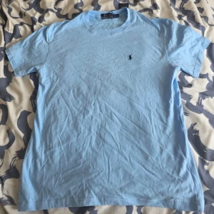 Ljusblå t-shirt från Ralph Lauren - Snygg ljusblå t-shirt från Ralph Lauren med klassisk passform och den ikoniska lilla loggan broderad på bröstet. sopassad för dig som gillar stilrena och enkla plagg. Perfekt till jeans eller shorts.