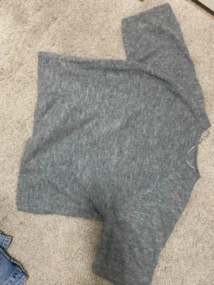 Grå stickad tröja i mjukt material - En enkel och stilren grå stickad tröja med kort ärm. Tröjan har en rak passform och är tillverkad i ett mjukt, tunt material som känns skönt mot huden. Perfekt att matcha med jeans eller kjol för en avslappnad look. Från lager 