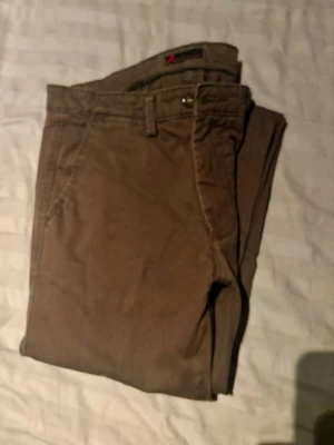 Bruna chinos med rak passform - Snygga bruna chinos med rak passform och klassiska sidofickor. Byxorna har bälteshällor och knappgylf. Perfekta för en clean och avslappnad stil. Tillverkade i mjukt bomullstyg som känns bekvämt hela dagen.