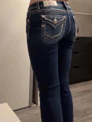 Miss Me bootcut jeans  - Snygga mörkblå jeans med bootcut passform och kontrastsömmar. Bakfickorna har detaljerat broderi och dekorativa knappar. Jeansen har låg midja och är tillverkade i klassiskt denimtyg. Längden passar för de som är runt 162-168. De är använda 2-3 ggr då jag tycker att de är för korta för mig som är 173