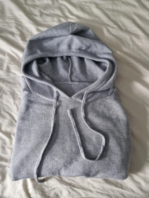 Kashmire hoodie  - En stilren ljusgrå hoodie med huva och dragsko. Tillverkad i mjukt, stickat material som känns skönt mot huden. Hoodien har klassisk passform och ribbade kanter vid huva och ärmslut. Perfekt för en avslappnad look. Står ingen storlek men den sitter som en XS.