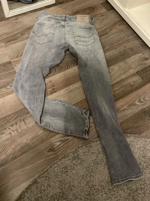 Grå tvättade jeans i rak modell - Säljer ett par grå tvättade jeans med klassisk femficksdesign och raka ben. Jeansen har en snygg slitningseffekt och normal midja. Perfekta till en avslappnad streetstil eller att matcha med en hoodie.