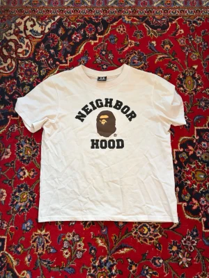 Vit BAPE t-shirt - Säljer en vit t-shirt från BAPE med klassiskt tryck på bröstet och rund hals. T-shirten har korta ärmar och är gjord i mjuk bomull. Perfekt för dig som gillar streetwear och vill sticka ut med en unik collab.