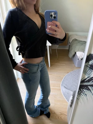 Svart omlottopp i manchester - Säljer en svart croppad omlottopp i manchester med långa ärmar och knyt i sidan. Toppen har en djup v-ringning och sitter snyggt figurnära. Perfekt till jeans eller kjol för en trendig look.