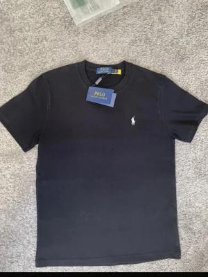 Svart t-shirt från Polo Ralph Lauren - Klassisk svart t-shirt från Polo Ralph Lauren med den ikoniska broderade loggan på bröstet. T-shirten har rund halsringning och korta ärmar. Tillverkad i mjuk bomull för en skön och stilren look.