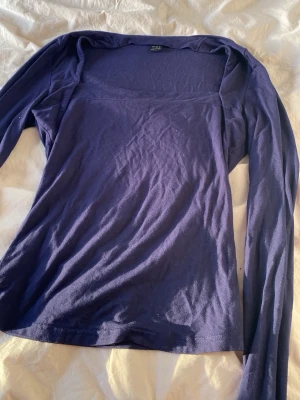 Mörklila långärmad topp - En enkel och stilren mörklila långärmad topp med rak skärning och mjukt material. Perfekt att matcha med jeans eller kjol för en clean look. Toppen har en något bredare urringning och är tillverkad i ett stretchigt tyg.