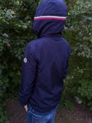  Moncler windbreaker - Snygg marinblå vindjacka från Moncler med huva och röd-vit rand längs huvan. Jackan har dragkedja framtill, två sidofickor och Moncler-logga på ärmen. Tillverkad i lätt, vindtätt material som passar perfekt till vår och höst.