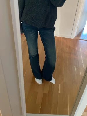 Blå bootcut jeans med tvättade detaljer - Säljer ett par blå bootcut jeans med snygga tvättade detaljer och lätt utsvängda ben. Jeansen har klassisk femficksdesign och låg midja. Perfekta för dig som gillar en avslappnad men trendig look.