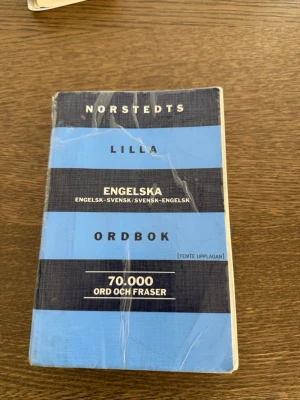 Norstedts lilla engelska ordbok - Praktisk engelsk-svensk/svensk-engelsk ordbok från Norstedts med 70 000 ord och fraser. Femte upplagan. Boken har blå och svarta ränder på omslaget och är i smidigt pocketformat, perfekt för studier eller resor.