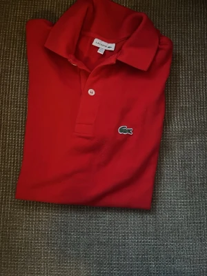 Röd pikétröja från Lacoste - Klassisk röd pikétröja från Lacoste med krage och två knappar framtill. 