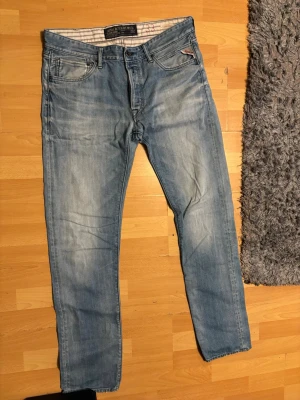 Ljusblå Replay jeans herr - Säljer ett par ljusblå jeans från Replay med klassisk femficksmodell och raka ben. Jeansen har snygga slitningar och detaljer vid fickorna samt en bekväm passform. Perfekta för en avslappnad och trendig stil.