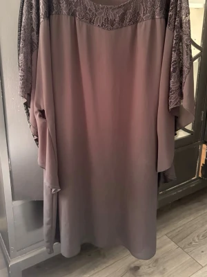 Svart långklänning med spets - Långklänning i helt svart med bred spets upptill och löst fall. Klänningen har ärmlös design och ett mjukt, flytande tyg som ger en elegant siluett. Perfekt för dig som gillar romantiska detaljer och en avslappnad look. Klänningen är i One-Size och är helt svart, det är bara ljuset på bilden som gör så att det ser ut så. Skriv för mått om det behövs.