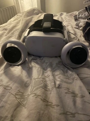 Oculus Quest 2 VR-headset med kontroller - Säljer ett Oculus Quest 2 VR-headset i vitt med tillhörande handkontroller. Headsetet har en justerbar svart huvudrem och är tillverkat i plast. Perfekt för dig som vill uppleva VR-spel och appar på ett smidigt och trådlöst sätt.