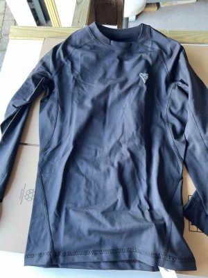  RDX T15 Rashguard Långärmad – Svart – Ny - Säljer en ny RDX T15 rashguard med lång ärm. Passar för BJJ, MMA, grappling, brottning och annan kampsportsträning. Fungerar både under gi och som träningströja för no-gi. Bekväm passform med god rörelsefrihet under träning. Oanvänd och i originalskick. Kan skickas eller hämtas efter överenskommelse. Hör gärna av dig vid intresse eller frågor.     