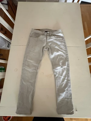 Ljusgrå slim fit jeans - Säljer ett par ljusgrå slim fit jeans från dondup med fem fickor och dragkedja. Jeansen har diskreta slitningar och kontrastsömmar på bakfickorna. Perfekta för en avslappnad och trendig look.