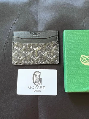 Svart kortfodral - Snyggt svart kortfodral med klassiskt mönster i vitt och grått. Fodralet har flera kortfack och är tillverkat i exklusivt läder och canvas. Perfekt för dig som vill ha en stilren och lyxig accessoar med ikonisk logga framtill.