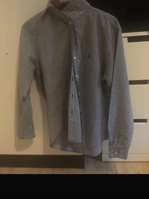 Rutig skjorta från Polo Ralph Lauren - Klassisk rutig skjorta från Polo Ralph Lauren i blått och vitt. Skjortan har lång ärm, knappar framtill och en liten broderad logga på bröstet. Tillverkad i mjuk bomull och passar perfekt till en avslappnad men ändå stilren look.