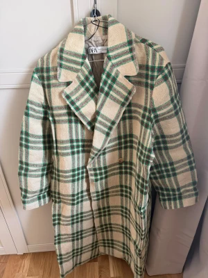 Rutigt beige och grönt linne kappa Zara - Stilren linne kappa från Zara i beige med grönt rutmönster. Dubbelknäppt med bred krage och fickor på sidorna. Tjockt linne tyg med slät innerfoder, perfekt för kyligare dagar. Oversized passform för en trendig look. Helt ny, använts endast en gång. Ny pris 1500kr