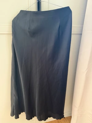 Svart långkjol i satin från Lager 157 - Säljer en svart långkjol från Lager 157 i glansigt satinmaterial. Kjolen har en enkel och elegant design med lätt utsvängd form och vågig nederkant. Perfekt att styla med både sneakers och klackar. Storlek M,  passar också perfekt till storlek S