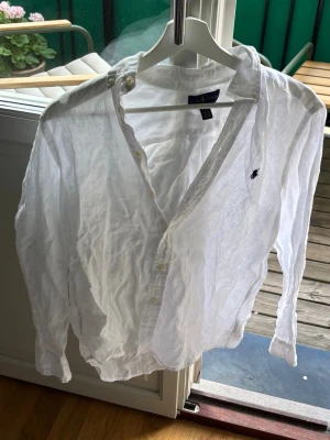 Vit linneskjorta från Ralph Lauren - Klassisk vit skjorta från Ralph Lauren i svalt linne. Skjortan har lång ärm, knappar framtill och den ikoniska broderade loggan på bröstet. Perfekt till sommaren och enkel att styla med allt. Snygg och tidlös design!
