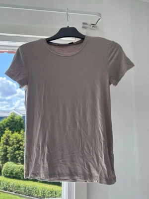 Beige basic t-shirt från 157 - En enkel och stilren beige t-shirt från 157 med rund halsringning och korta ärmar. Tillverkad i mjuk bomull som känns skön mot huden. Perfekt att matcha med jeans eller shorts för en clean look. (Aldrig använd) 