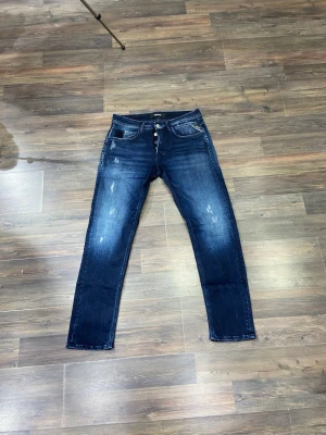  Replay jeans - Snygga mörkblå slim fit jeans från Replay med slitna detaljer och klassiska fem fickor. Jeansen har en knappgylf och kontrastsömmar. Materialet är denim i bomull med lite stretch för extra komfort. Perfekta för en trendig och avslappnad look.