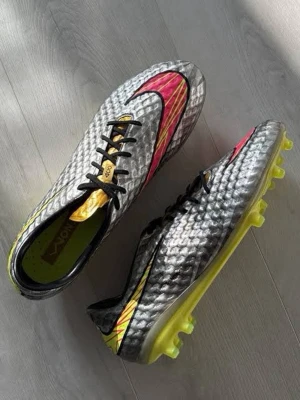 Nike Hypervenom Neymar silver - Snygga fotbollsskor från Nike i silver med svart snörning, neonfärgade detaljer i gult och rosa samt svart swoosh. Skorna har en texturerad ovandel för bättre bollkontroll och gula dobbar för bra grepp på planen. Perfekta för dig som vill sticka ut på matchen.