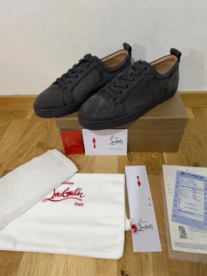Grå Christian Louboutin  - Snygga gråa sneakers från Christian Louboutin i mocka med klassisk röd sula. Skorna har lågt skaft, matchande grå skosnören och diskret design. Perfekta för dig som gillar exklusiva detaljer och vill sticka ut med en ikonisk röd undersida.TVEKA INTE ATT SKICKA EN BUD:)