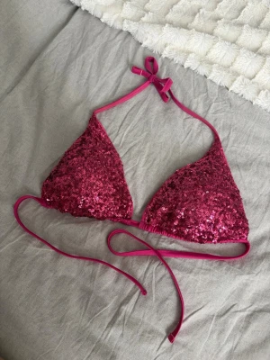 Calzedonia rosa paljettbikini triangel - Säljer en superfin trekantsbikini i stark rosa med glittrande paljetter. Bikinin har tunna band som knyts i nacken och runt ryggen för justerbar passform. Perfekt för dig som vill sticka ut på stranden eller poolpartyt!